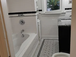Freshly cleaned bathroom with white tile and black accents.