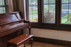 Shiny wooden piano next to dark brown wooden windows and a freshly mopped wooden floor.
