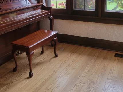 Shiny wooden piano next to dark brown wooden windows and a freshly mopped wooden floor.