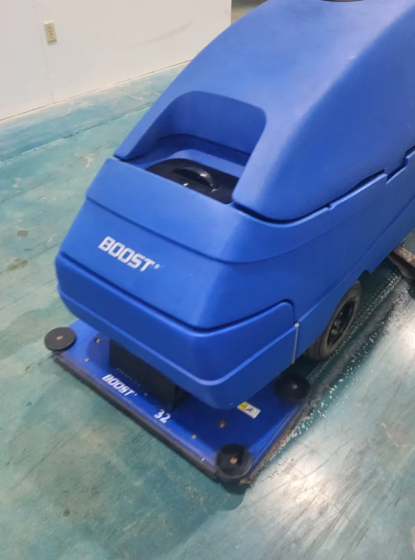 Commercial floor scrubbing machine cleaning the floor of a shipping warehouse.