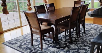 A freshly vacuumed blue rug with a dark brown and worn dining room table after a routine clean.