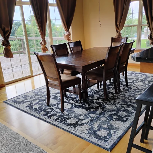 A freshly vacuumed blue rug with a dark brown and worn dining room table after a routine clean.