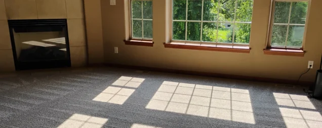 Clear vacuum lines on a gray carpet in a large living room after a move-out clean.