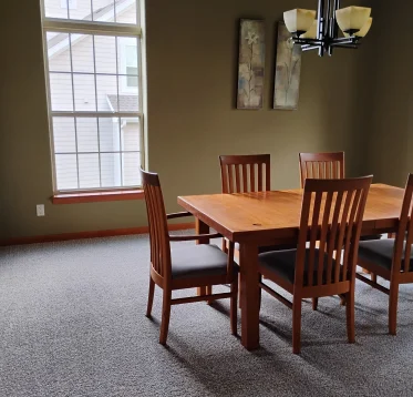 Tidy dining room with a gray carpet and brown wooden dining table, after a routine cleaning.