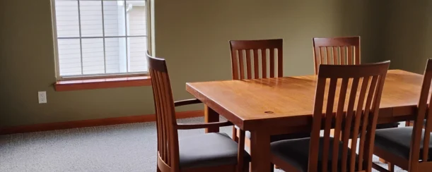 Tidy dining room with a gray carpet and brown wooden dining table, after a routine cleaning.